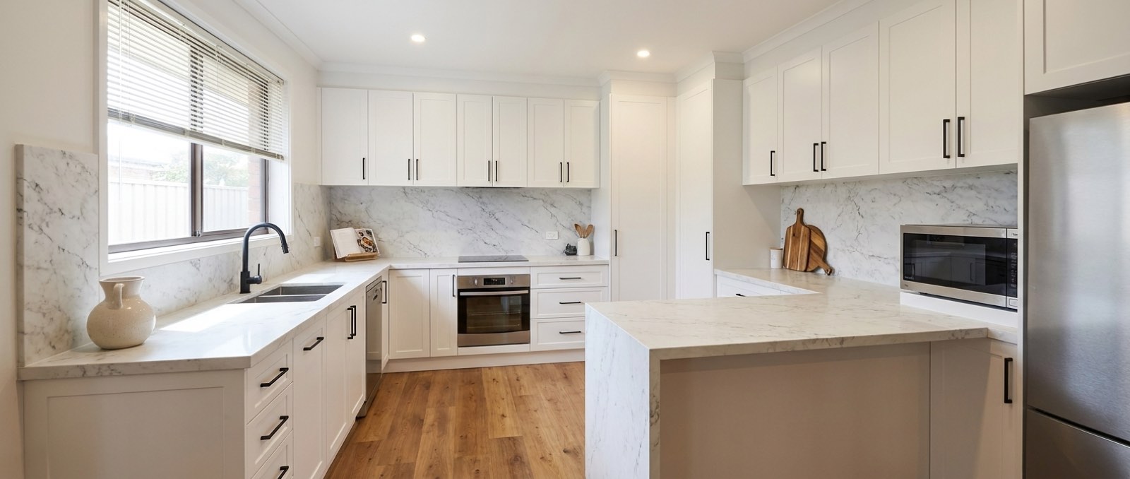 The same kitchen after renovation with white shaker cabinetry and stone benchtops